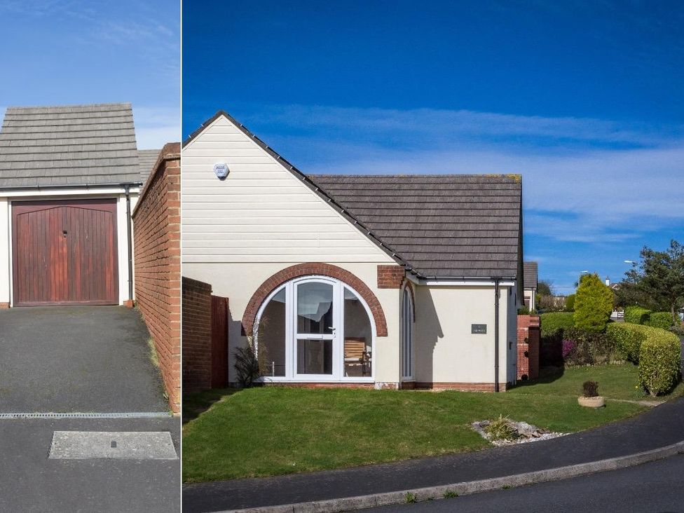 A bungalow with a sloped roof garage and arched window next to a garden with trimmed bushes at Fairways Woolacombe