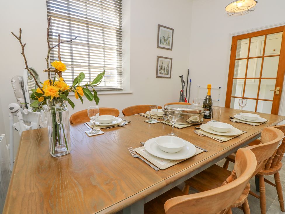 A dining room with a wooden table set for six with plates glasses and a flower vase at The Coach House in Wroxall