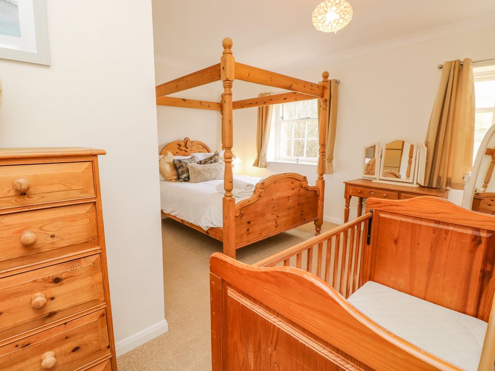 A bedroom with a wooden four poster bed a wooden crib a wooden dresser and a wooden vanity at The Coach House in Wroxall