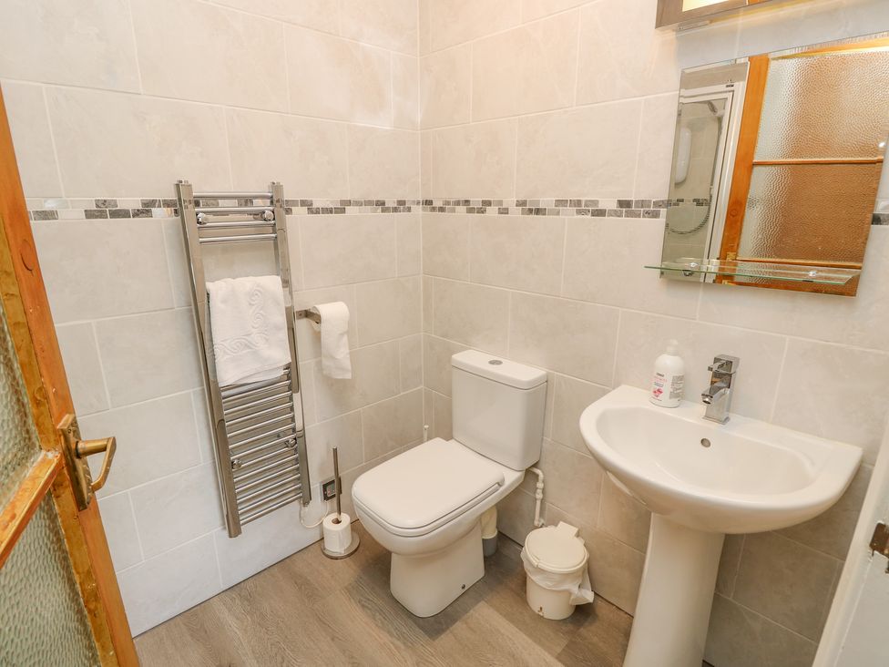 A bathroom with a toilet sink mirror towel rack and a small trash bin at The Coach House in Wroxall