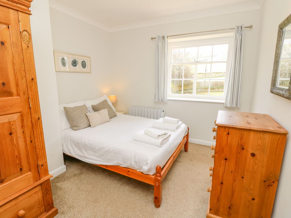 A bedroom with a wooden bed frame a wooden wardrobe a wooden chest of drawers and a window at The Coach House Wroxall