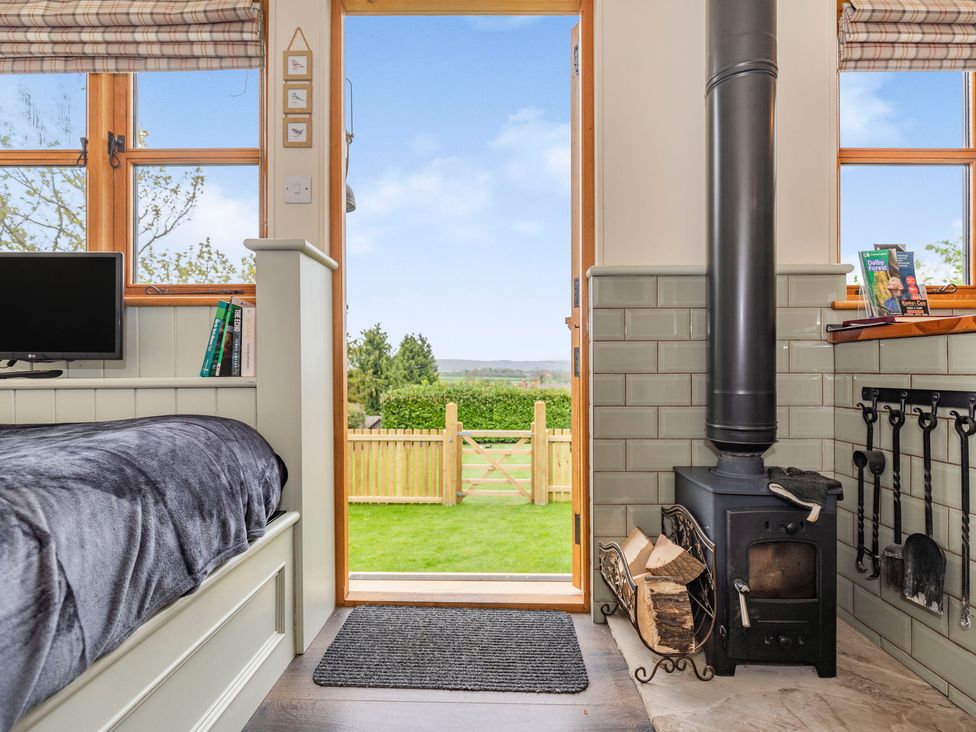 A small room with a black wood stove next to a bed and an open door leading to a garden at The Brae in Snainton