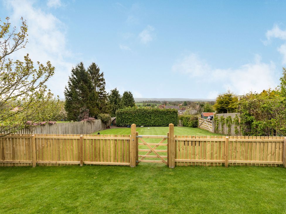 A backyard with a wooden fence a gate green grass trees and shrubs at The Brae in Snainton