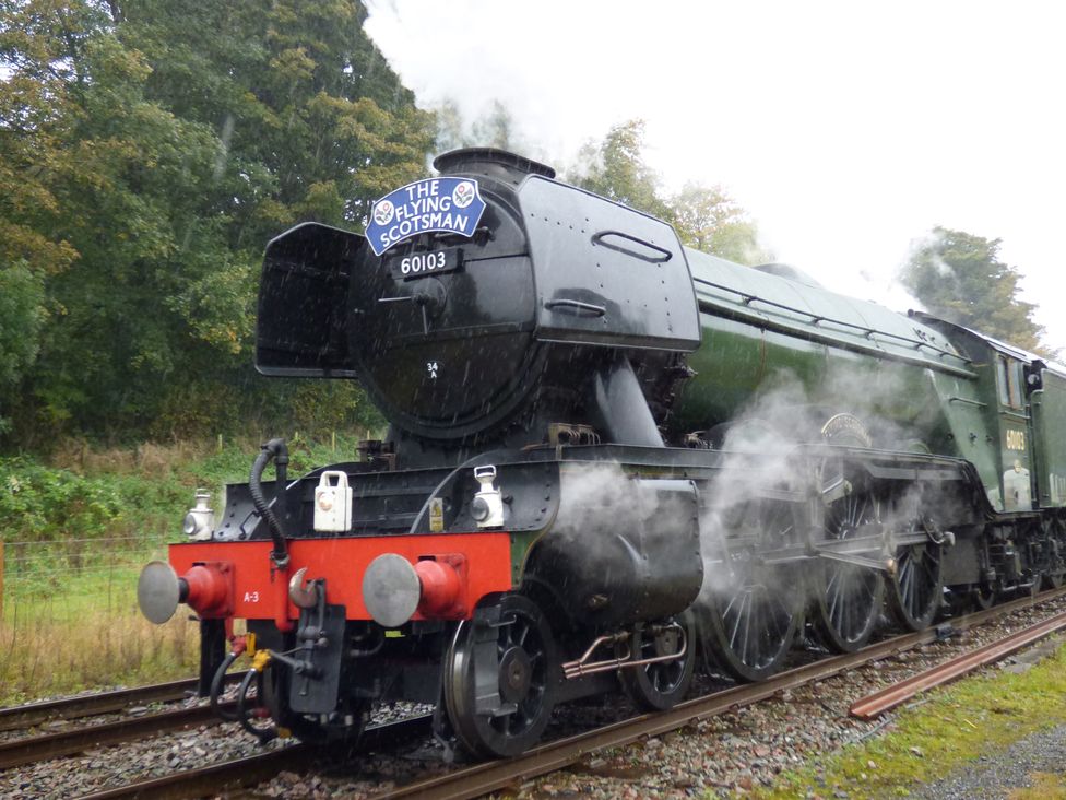 A black and green steam locomotive with the sign the flying scotsman on railway tracks near trees at Angel Cottage in Skipton