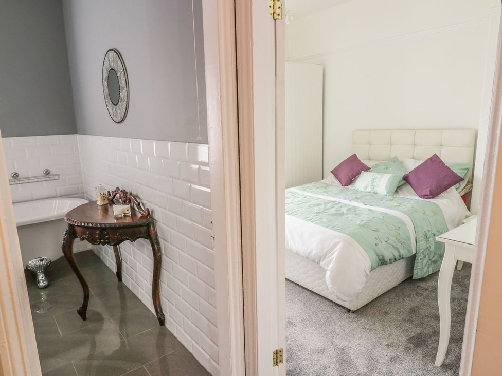 A bathroom with a bathtub and wooden table next to a bedroom with a bed and a bedside table at Angel Cottage in Skipton