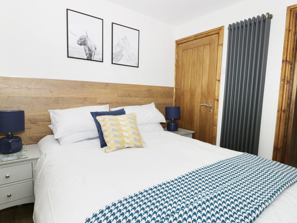 A bedroom with a double bed white bedding and blue patterned throw with wooden headboard and door at Fieldside in Hunmanby