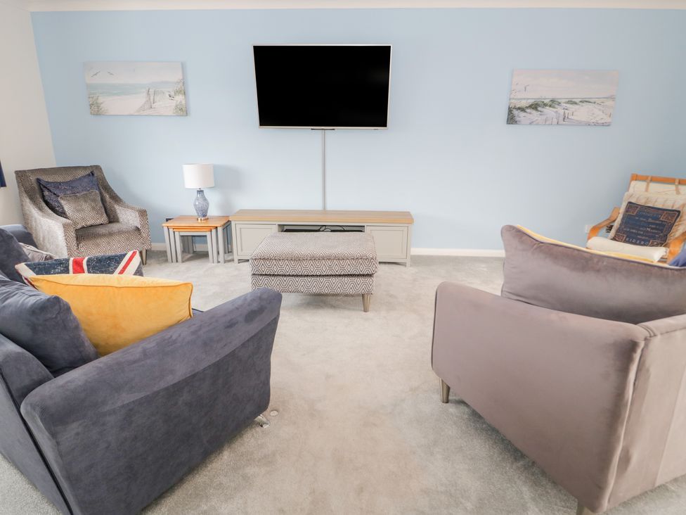 A living room with a wall mounted tv armchairs a sofa an ottoman and a side table with a lamp at Bay Lodge in Bull Bay