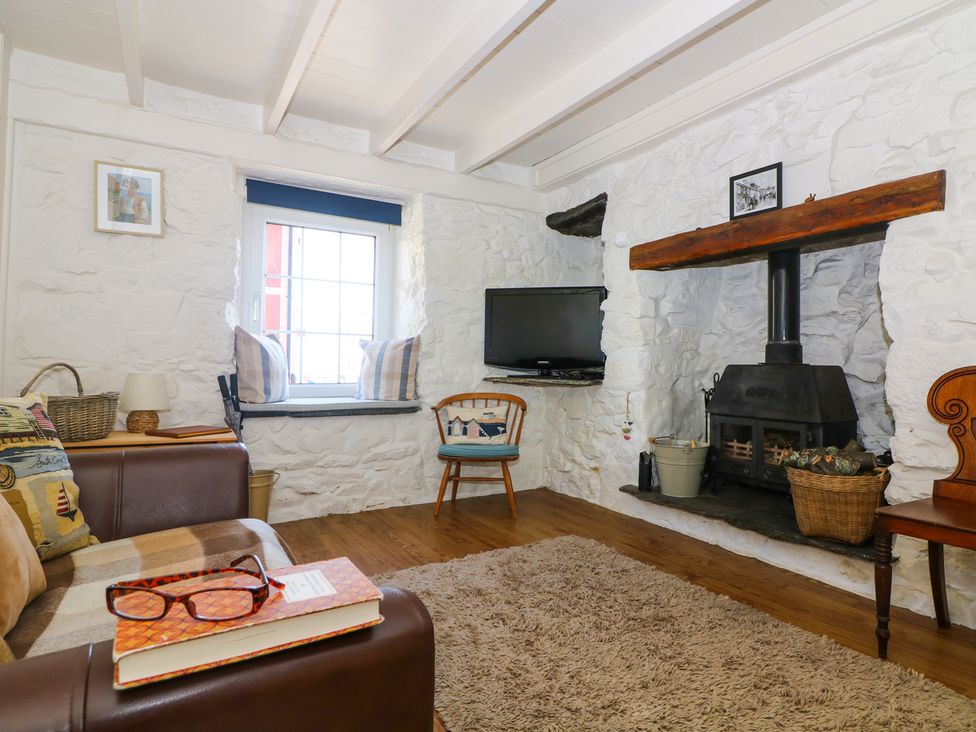 A living room with a stone fireplace a television a wooden chair and a sofa at Ner Sea in Marazion