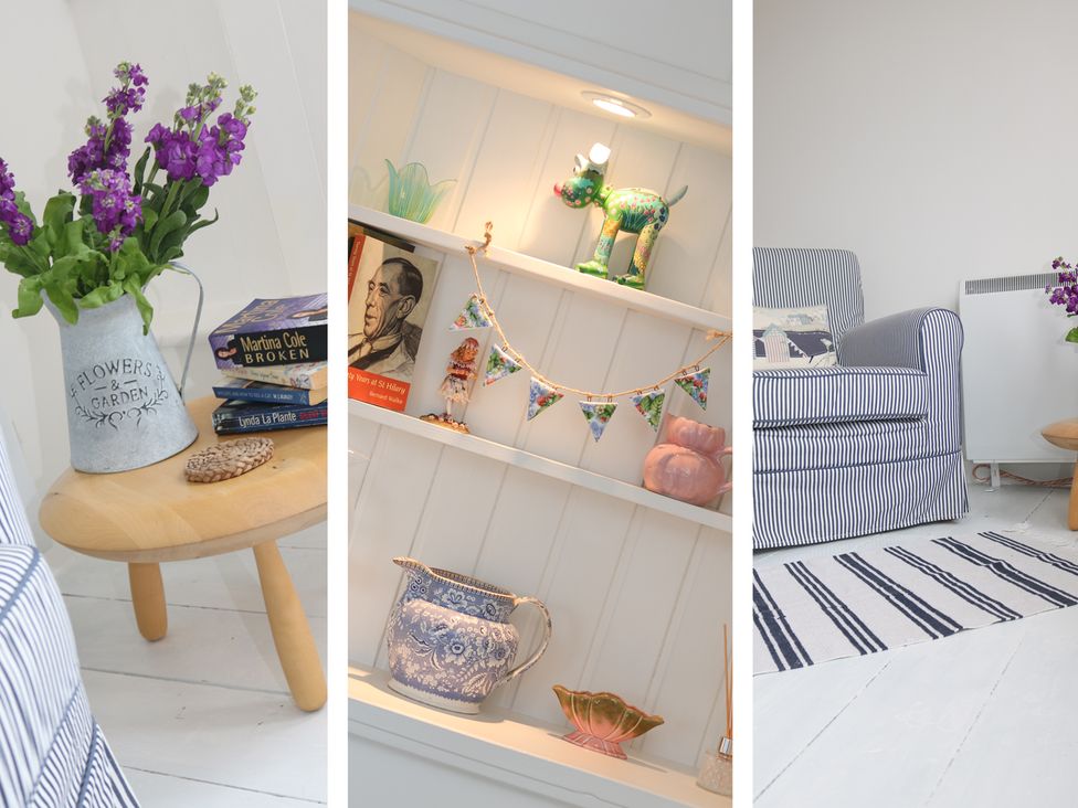A striped armchair next to a small wooden table with flowers and books near a shelf with decorations at Ner Sea in Marazion