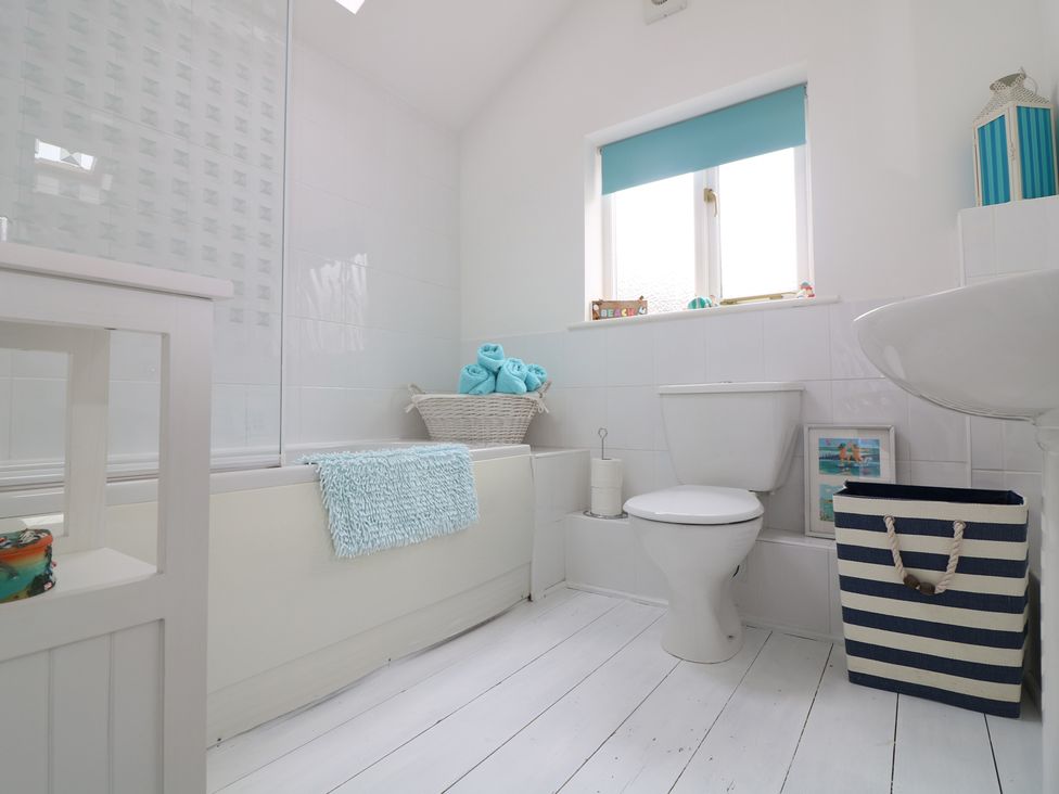 A bathroom with a bathtub a toilet a sink a basket with towels and a striped laundry basket at Ner Sea in Marazion