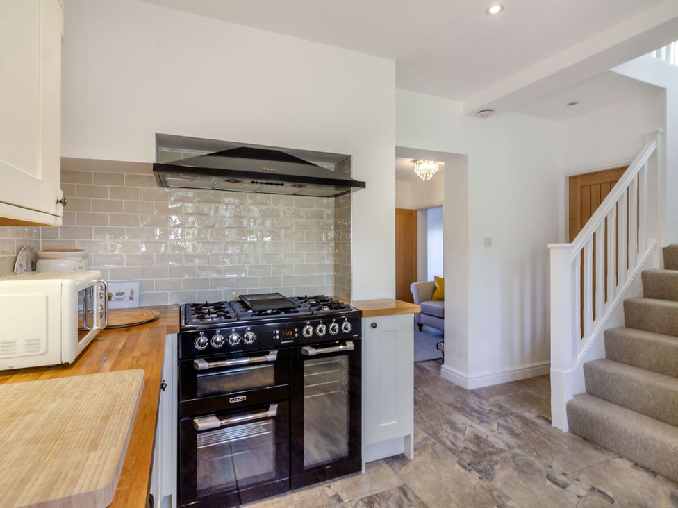 A kitchen with a black oven and stove a white microwave wooden countertops and a staircase carpeted stairs at Galen Croft in Curbar