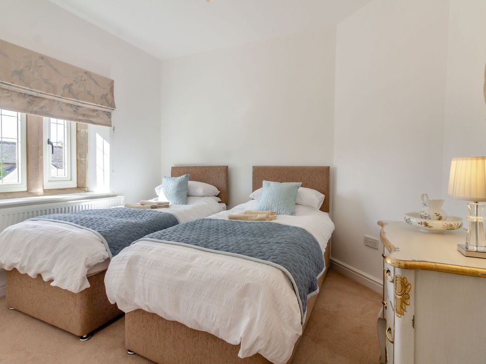 A bedroom with two single beds and a dresser with a lamp at Galen Croft in Curbar