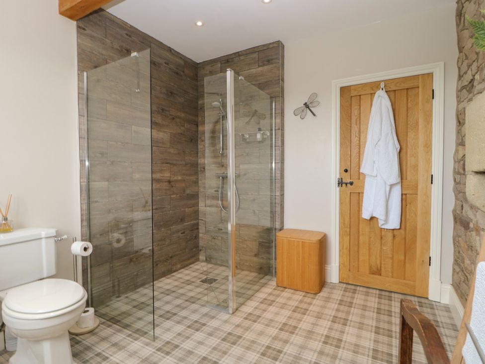 A bathroom with a walk in shower with glass panels a wooden door a white toilet and a wooden hamper at Cuthbert Hill Farm in Chipping