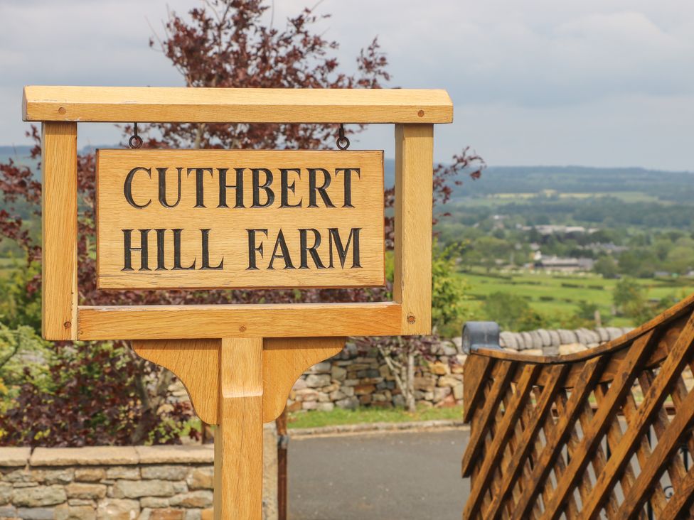 A wooden sign reading Cuthbert Hill Farm with a stone wall and countryside in the background at Cuthbert Hill Farm in Chipping