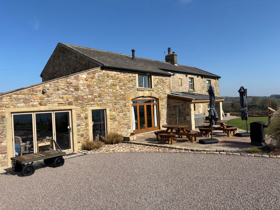 An outdoor view of a stone house with picnic tables and umbrellas on the patio at Cuthbert Hill Farm in Chipping