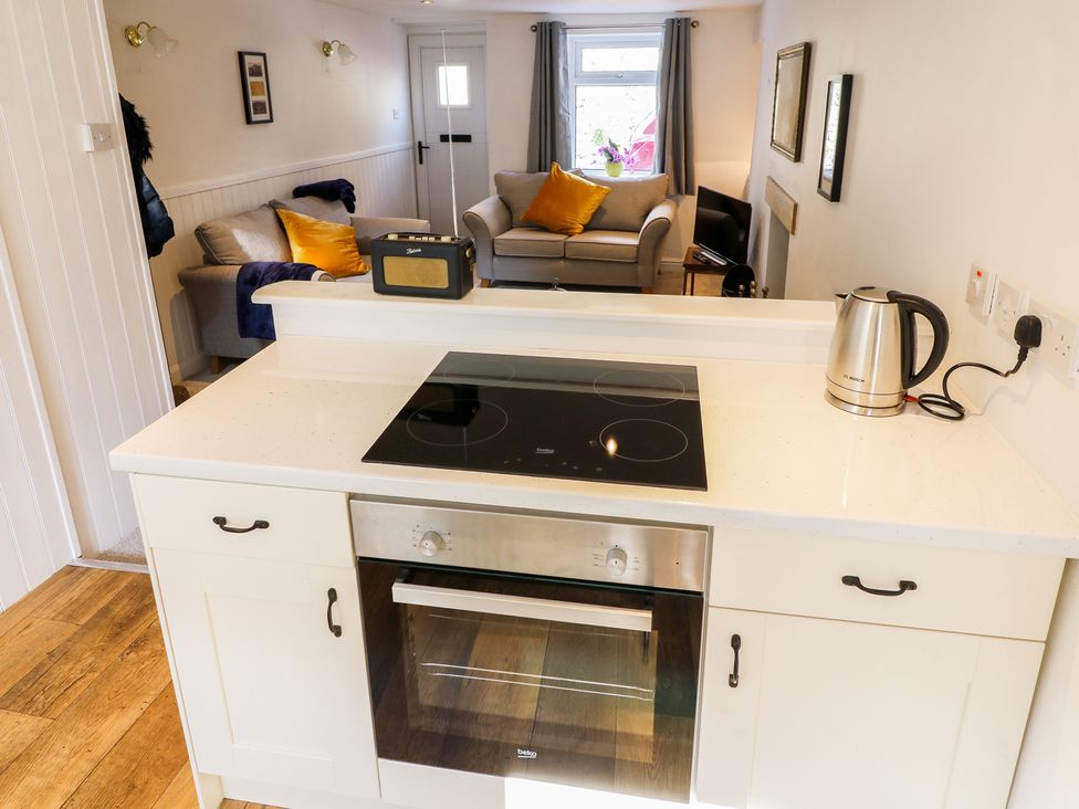 A kitchen counter with a stovetop and kettle overlooking a living room with two sofas and cushions at Copper Cottage in Ingleton