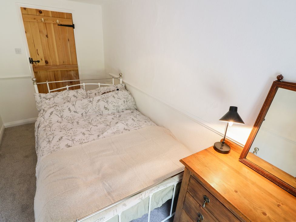 A bedroom with a bed a wooden door a wooden dresser with a lamp and a mirror at Copper Cottage in Ingleton