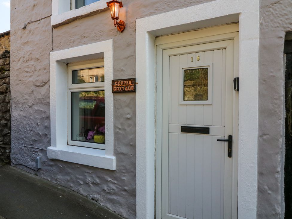 The front door and window of Copper Cottage with a lamp above the door and a sign next to the window in Ingleton