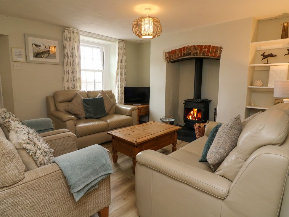 A living room with a fireplace two sofas an armchair a wooden coffee table and a window at Pheasant Cottage in Ilfracombe