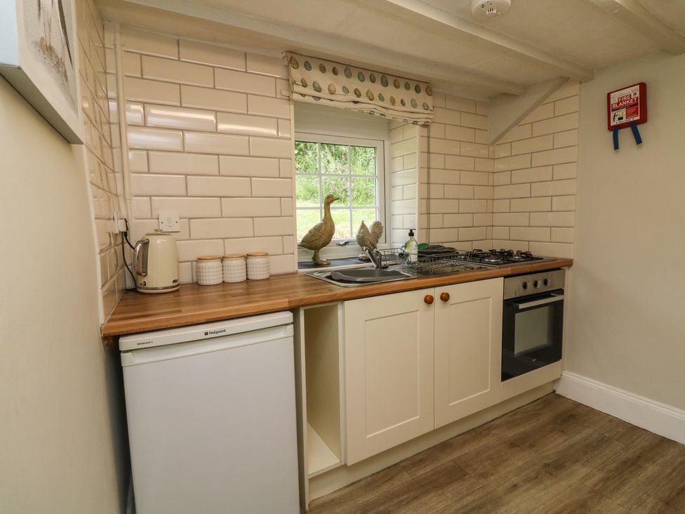 A kitchen with a fridge kettle jars sink stove oven and window with decorative duck at Pheasant Cottage in Ilfracombe