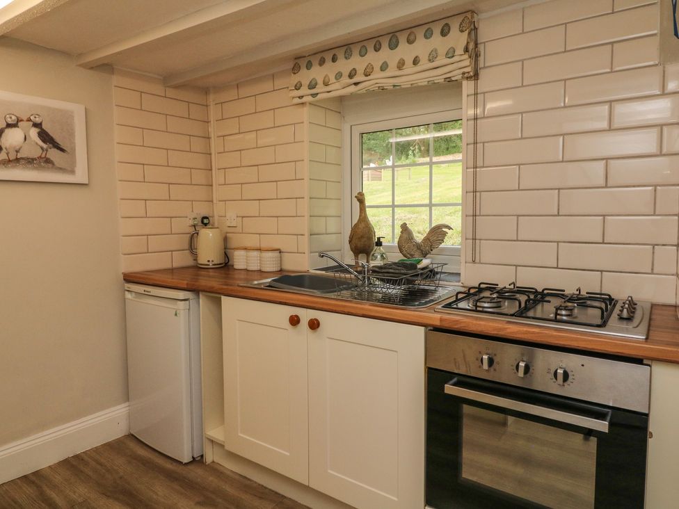A kitchen with a countertop sink stove oven small refrigerator and window at Pheasant Cottage in Ilfracombe