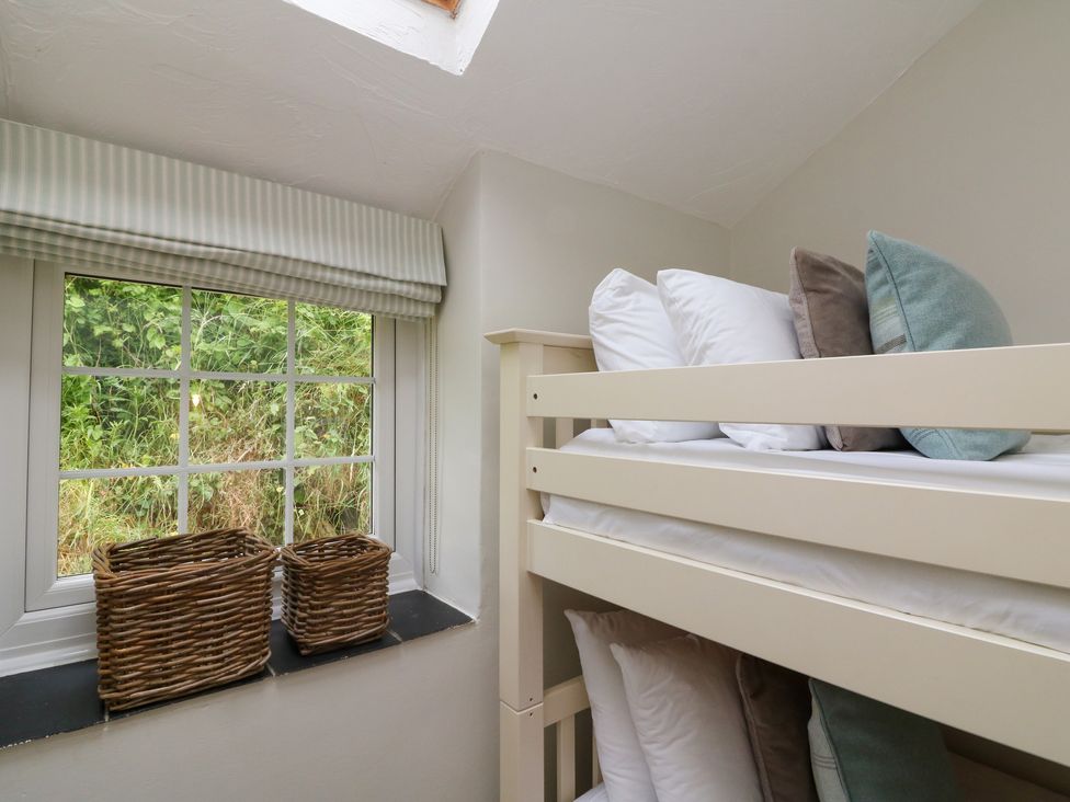 A bedroom corner with a bunk bed next to a window with baskets on the windowsill at Pheasant Cottage in Ilfracombe