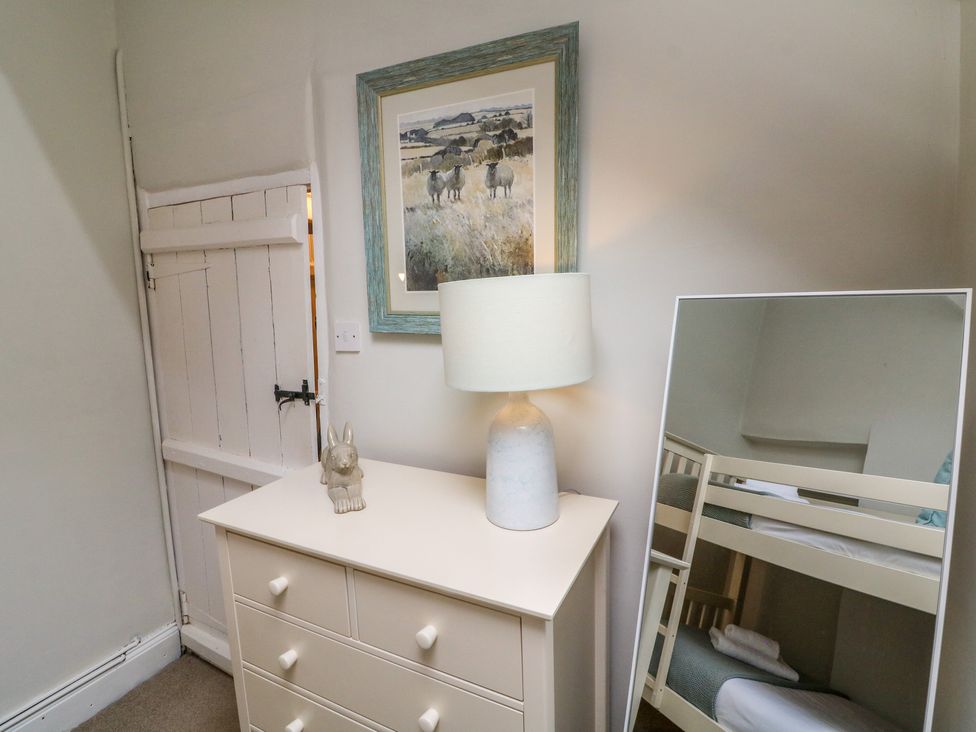 A bedroom corner with a dresser lamp and figurine next to a mirror reflecting bunk beds at Pheasant Cottage in Ilfracombe