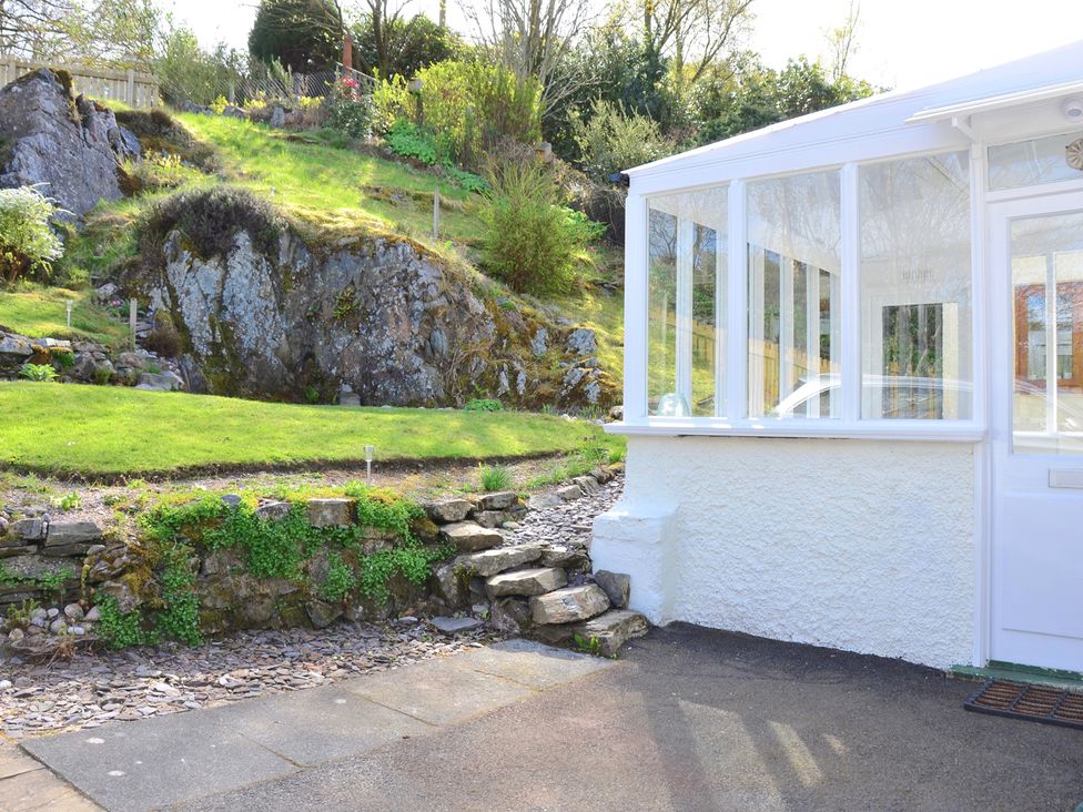 A garden with stone steps leading up to a grassy area next to a white conservatory at Ling Fell Cottage in Backbarrow