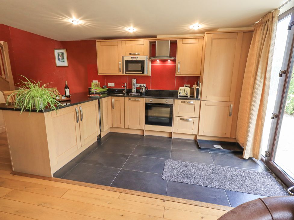 A kitchen with wooden cabinets black countertops and red walls at Stonegarth Mews in Grasmere
