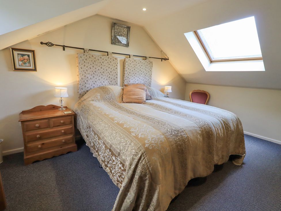 A bedroom with a large bed a wooden nightstand with lamps a skylight window and a chair at Stonegarth Mews in Grasmere