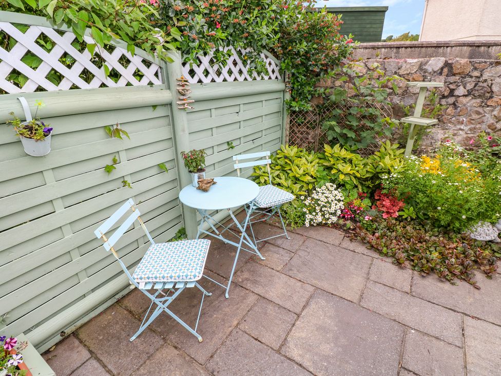An outdoor patio with two chairs and a small table near a green fence and a flower bed at Castle School House in Kidwelly
