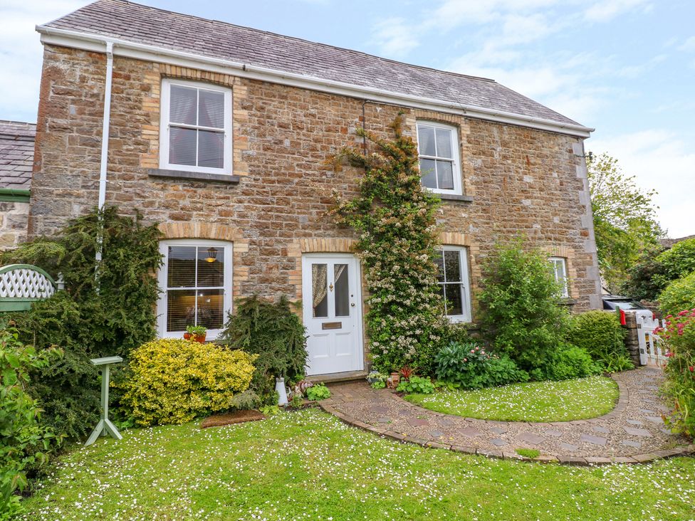 The front of a stone house with a white door and four windows surrounded by green bushes and a stone path leading to the door at Castle School House in Kidwelly