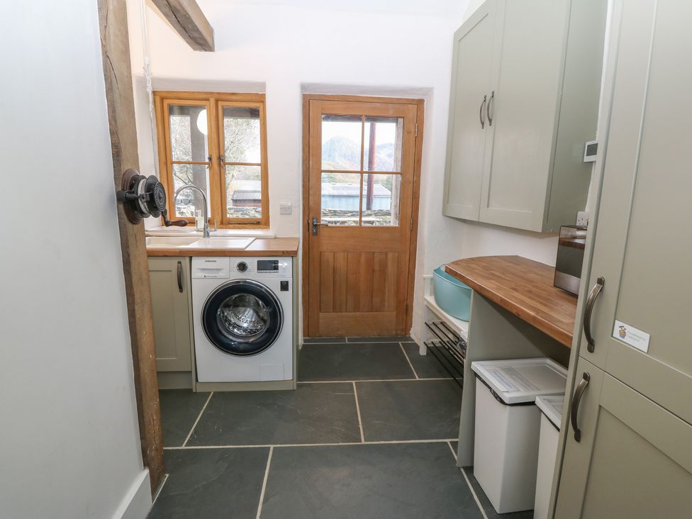 A utility room with washing machine wooden countertop cabinets and a wooden door at Peniarth Ganol in Tywyn