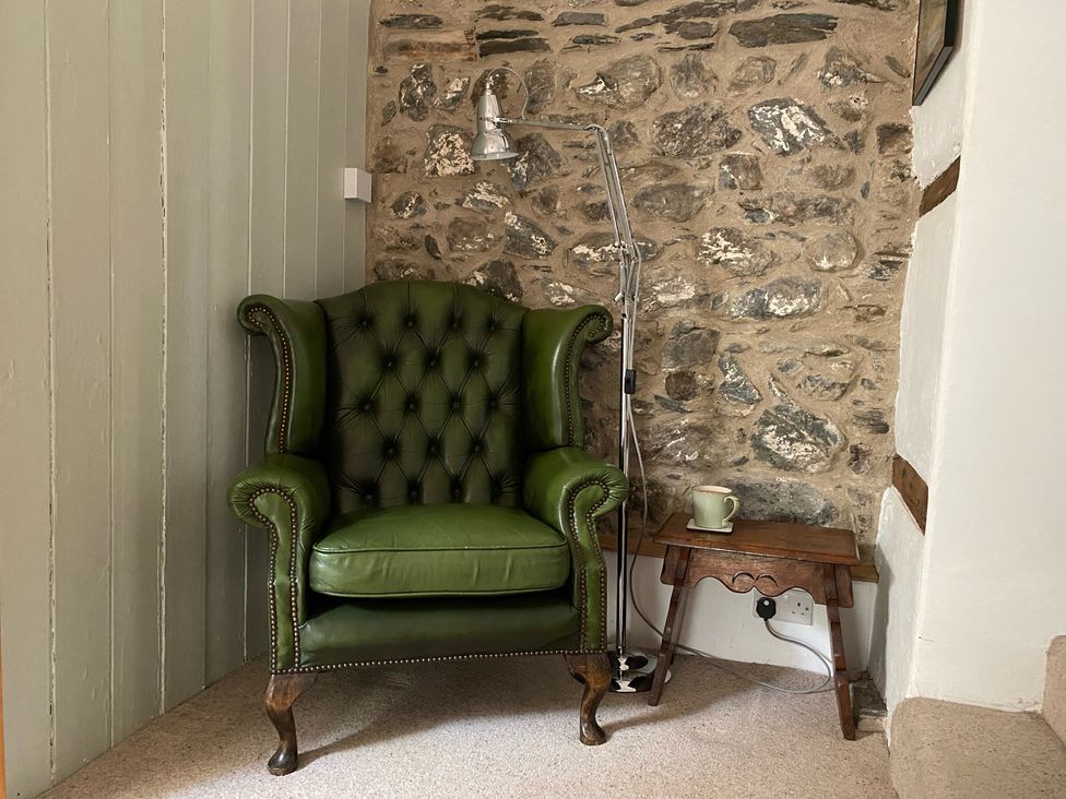 A green armchair next to a small wooden table with a mug and a standing lamp beside a stone wall at Peniarth Ganol in Tywyn