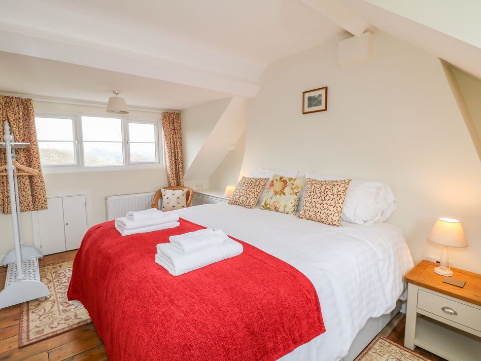 A bedroom with a large bed covered with white sheets and a red blanket with pillows two bedside tables with lamps a window with curtains and a cushioned chair at Wyebrow Cottage in Bakewell