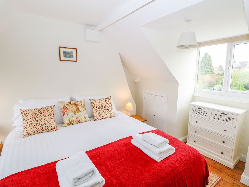 A bedroom with a bed with red and white bedding pillows a dresser and window at Wyebrow Cottage in Bakewell