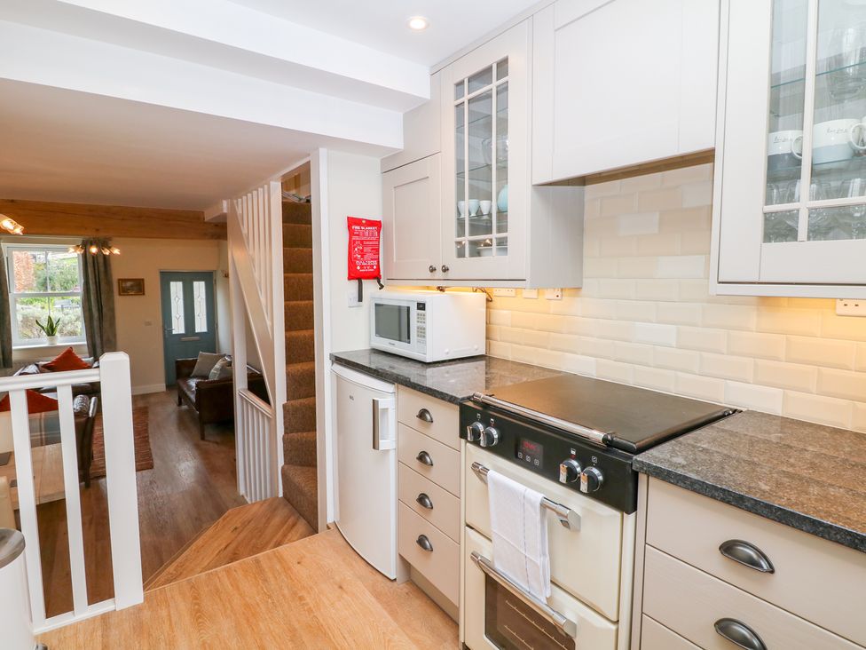 A kitchen with an oven microwave refrigerator and cabinets next to a carpeted staircase and a living room in the background at Wyebrow Cottage in Bakewell