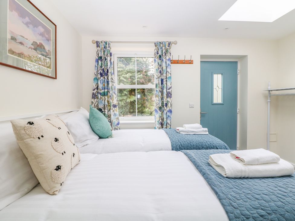 A bedroom with two single beds with blue bed runners and white towels near a window with floral curtains at Wyebrow Cottage in Bakewell