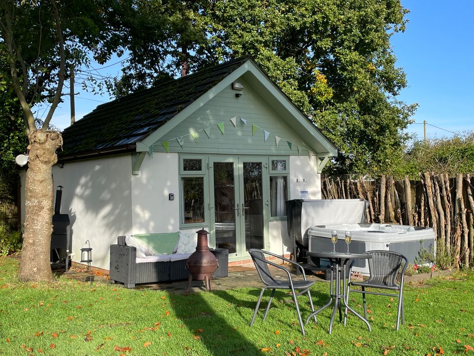 A small building with outdoor furniture a hot tub and bunting in a garden at Pheasant Lodge in Wimborne Minster