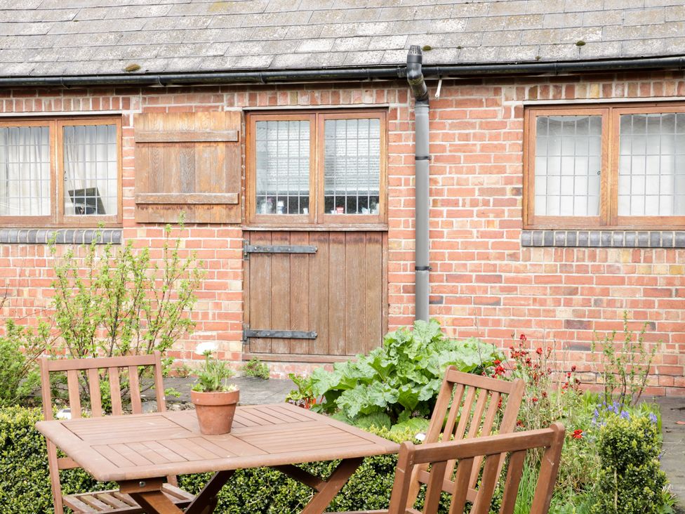 A wooden table with chairs and a potted plant outside a brick building with wooden windows and a door at Acorn Cottage 1 Burlton near Ellesmere