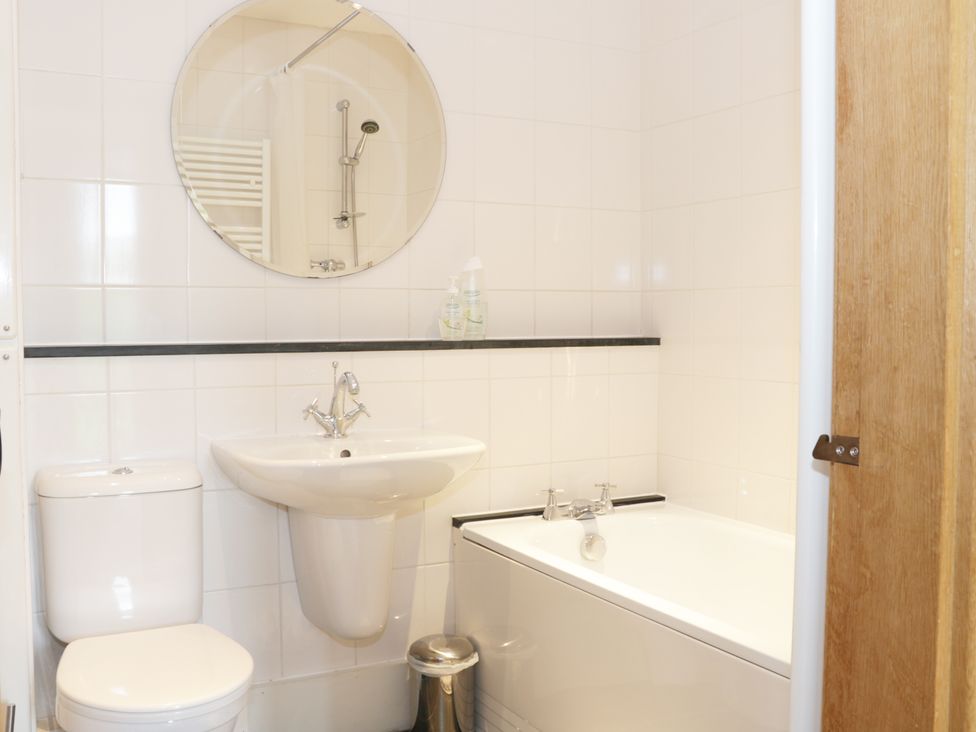 A bathroom with a toilet a sink a round mirror a bathtub and a wooden door at Acorn Cottage 1 Burlton near Ellesmere