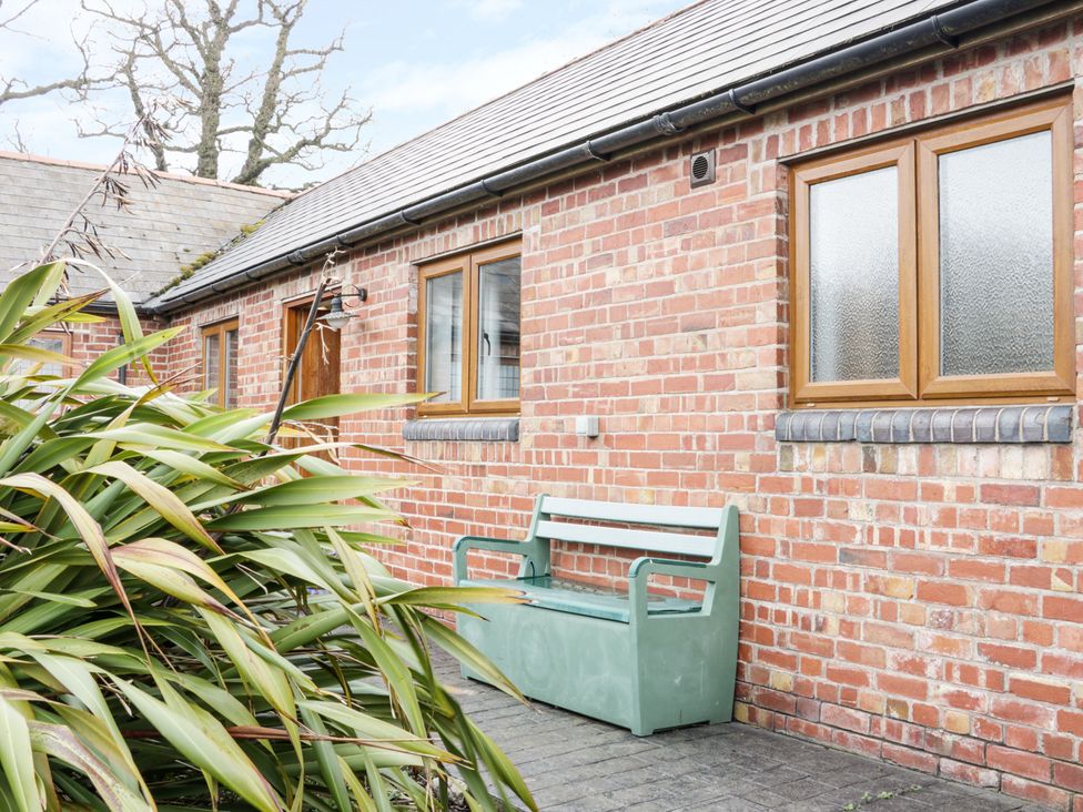 A brick building with four windows and a door with a green bench outside near plants at Acorn Cottage 1 Burlton near Ellesmere