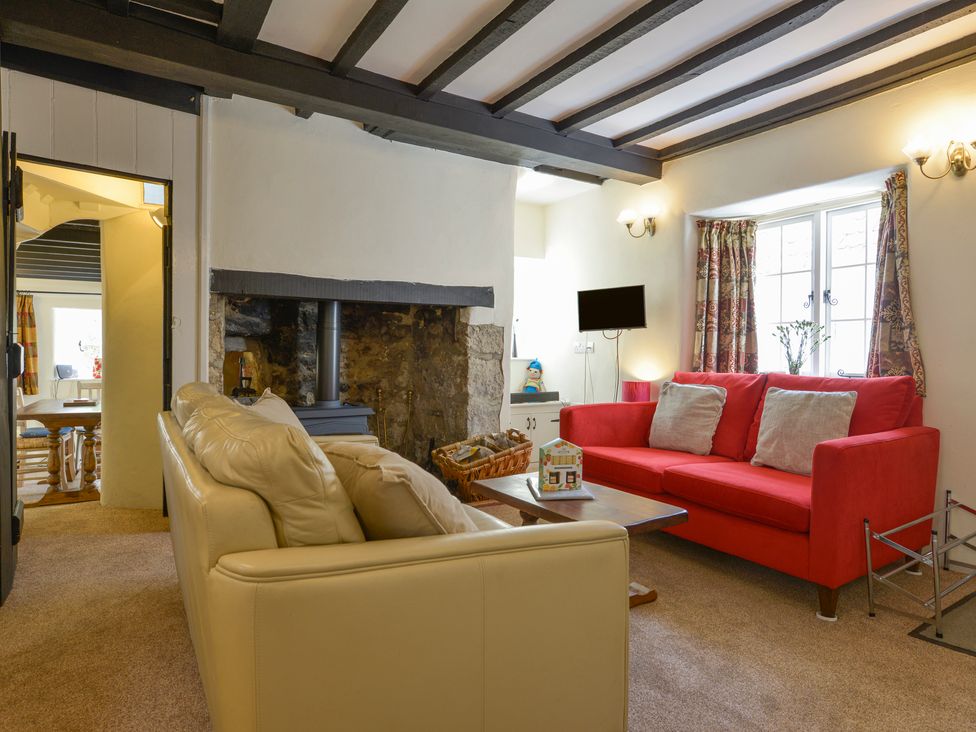 A living room with a beige sofa a red sofa a wooden coffee table and a fireplace at Little Gate Cottage in North Bovey