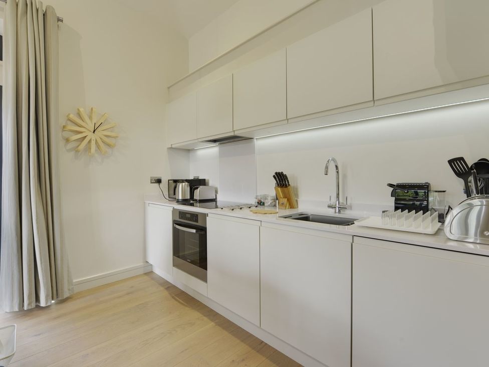 A kitchen with white cabinets sink oven and cooking utensils at Grooms Cottage in Talaton near Ottery St Mary