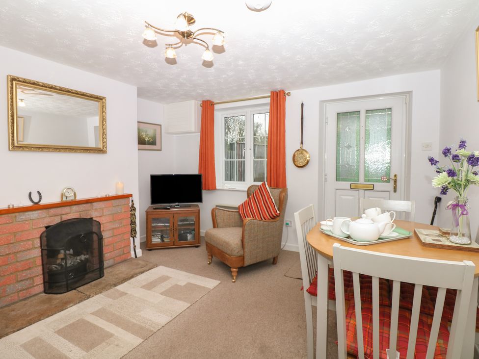 A living room with a fireplace armchair dining table with tea set and flowers at Poppy Cottage in Charlton Marshall