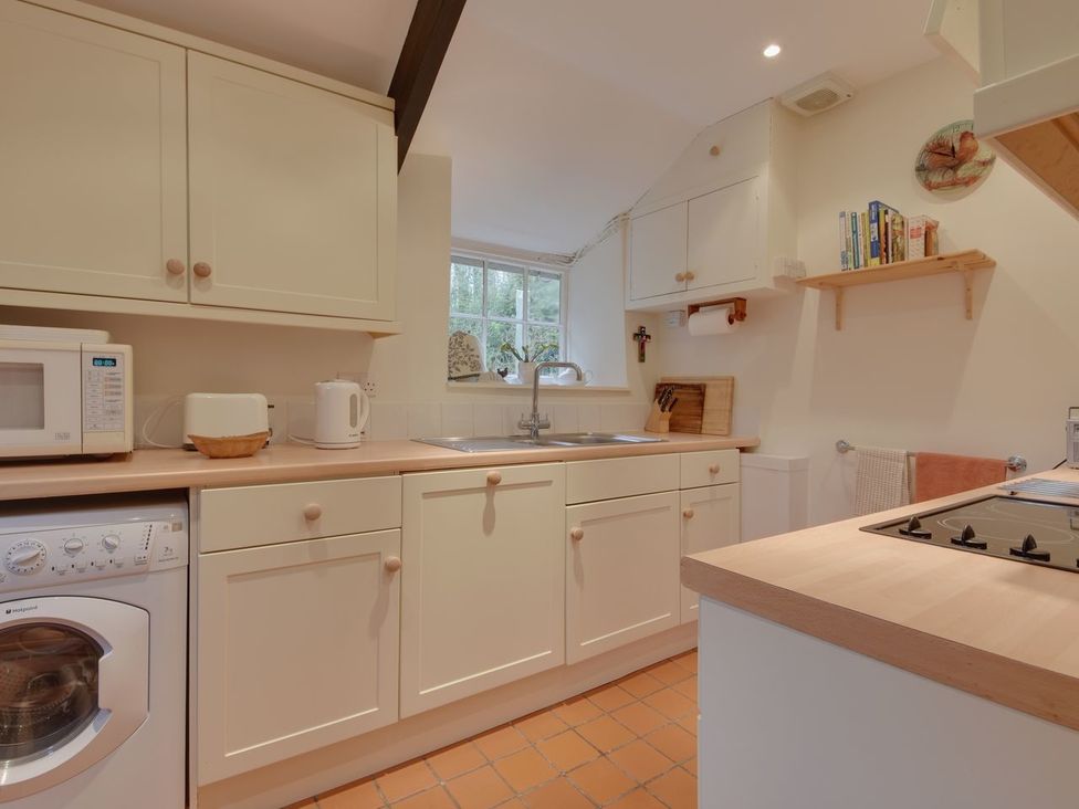 A kitchen with cream cabinets a washing machine microwave toaster kettle sink and stove at Lew Quarry Cottage Lewdown