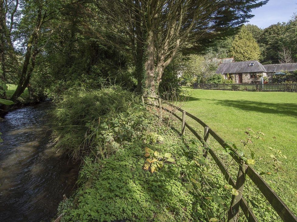 A small stream next to a wooden fence and a stone house with a garden at Honey House in Combebow near Bridestowe