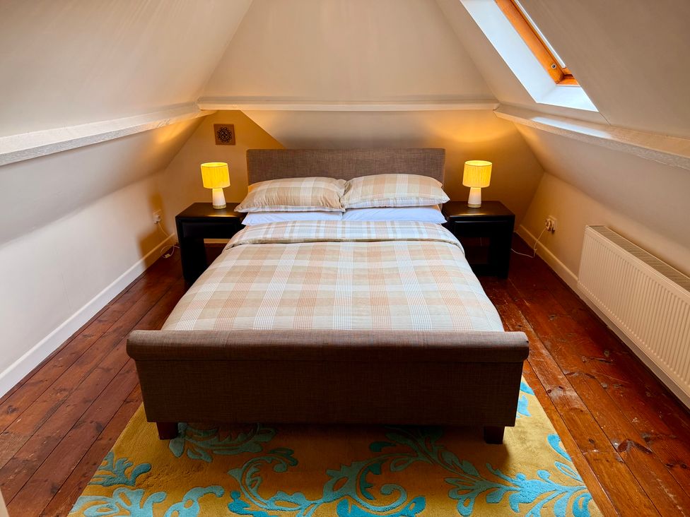 A bedroom with a double bed two bedside tables with lamps a skylight and a patterned rug at Honey House in Combebow near Bridestowe