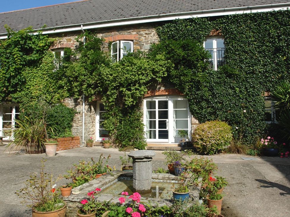 An outdoor courtyard with a stone building covered in ivy and a small water fountain surrounded by potted plants at The Gallery in Aveton Gifford