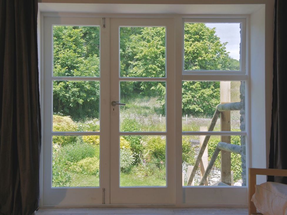 A window with glass panes overlooking a garden with green trees at The Gallery in Aveton Gifford